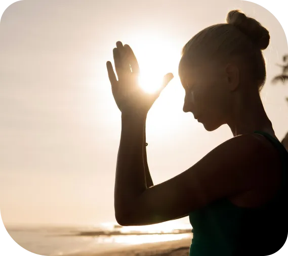 A woman at sunrise with hands together, reflecting